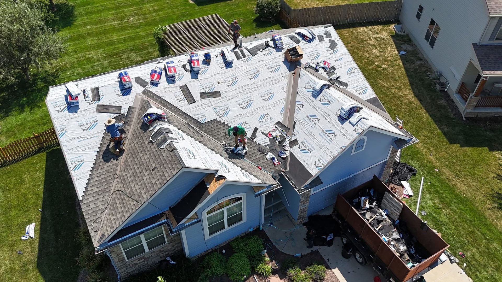 Aerial view of a house undergoing roof replacement with workers and materials spread across the roof.