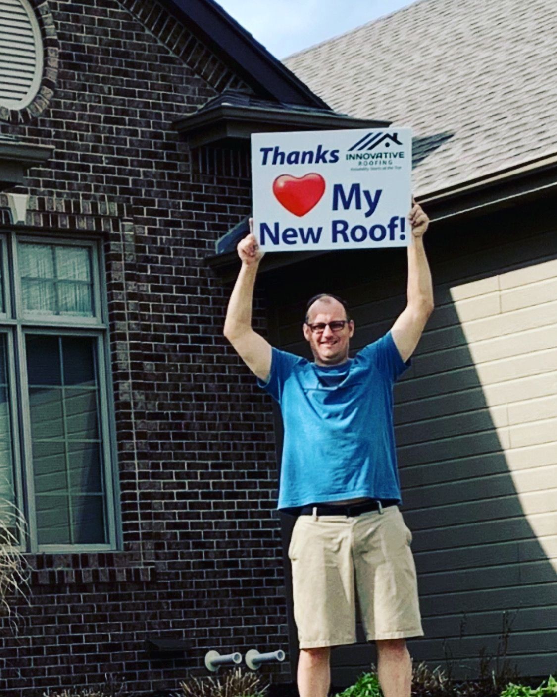 Man standing in front of a house holding a sign saying 'Thanks ❤ My New Roof!'