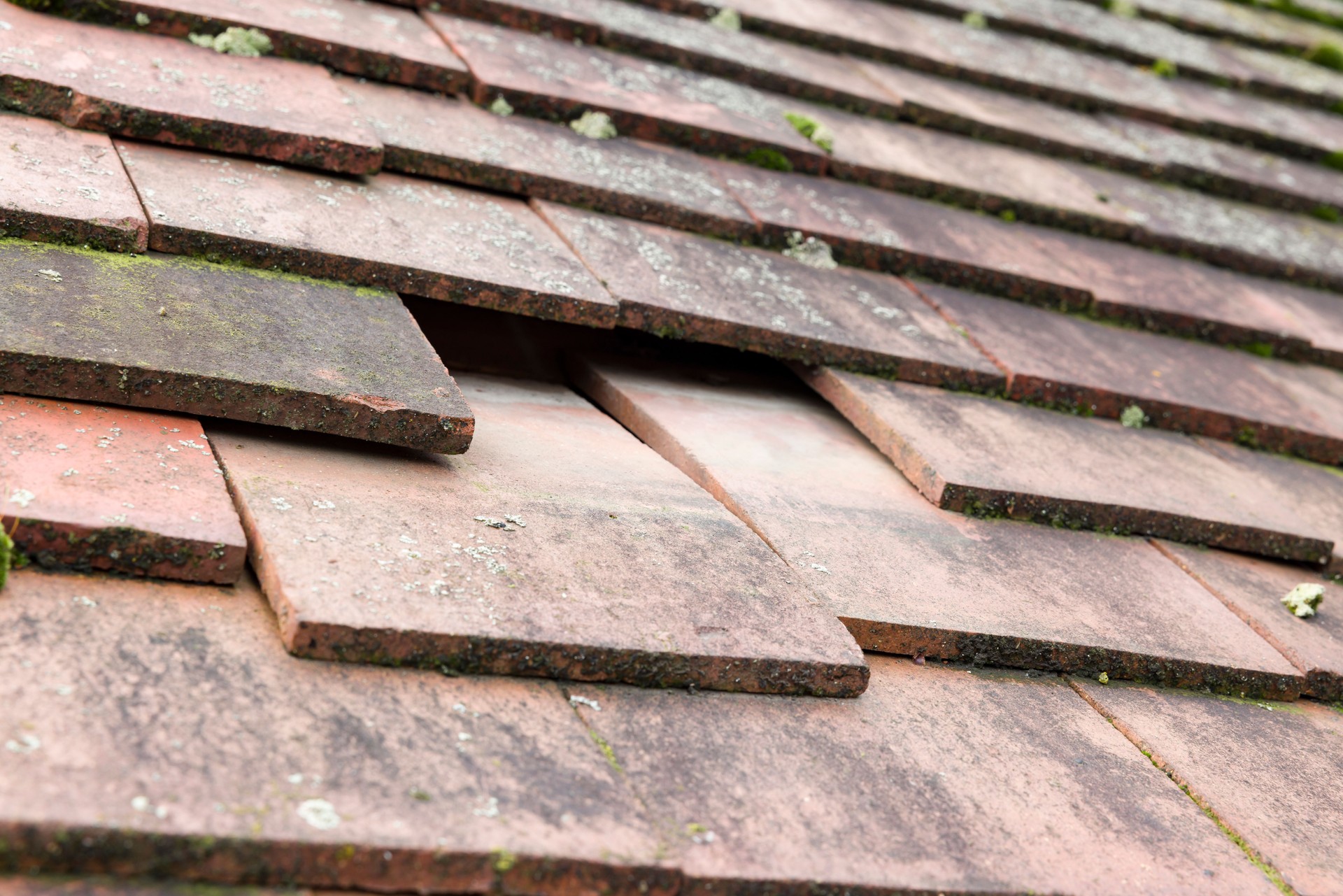 Missing and slipped plain clay roof tiles on a house roof, UK