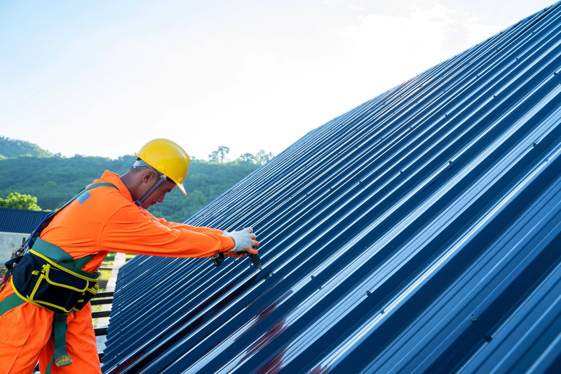 Roofer worker in special protective work wear use electric drill installing new roofs.